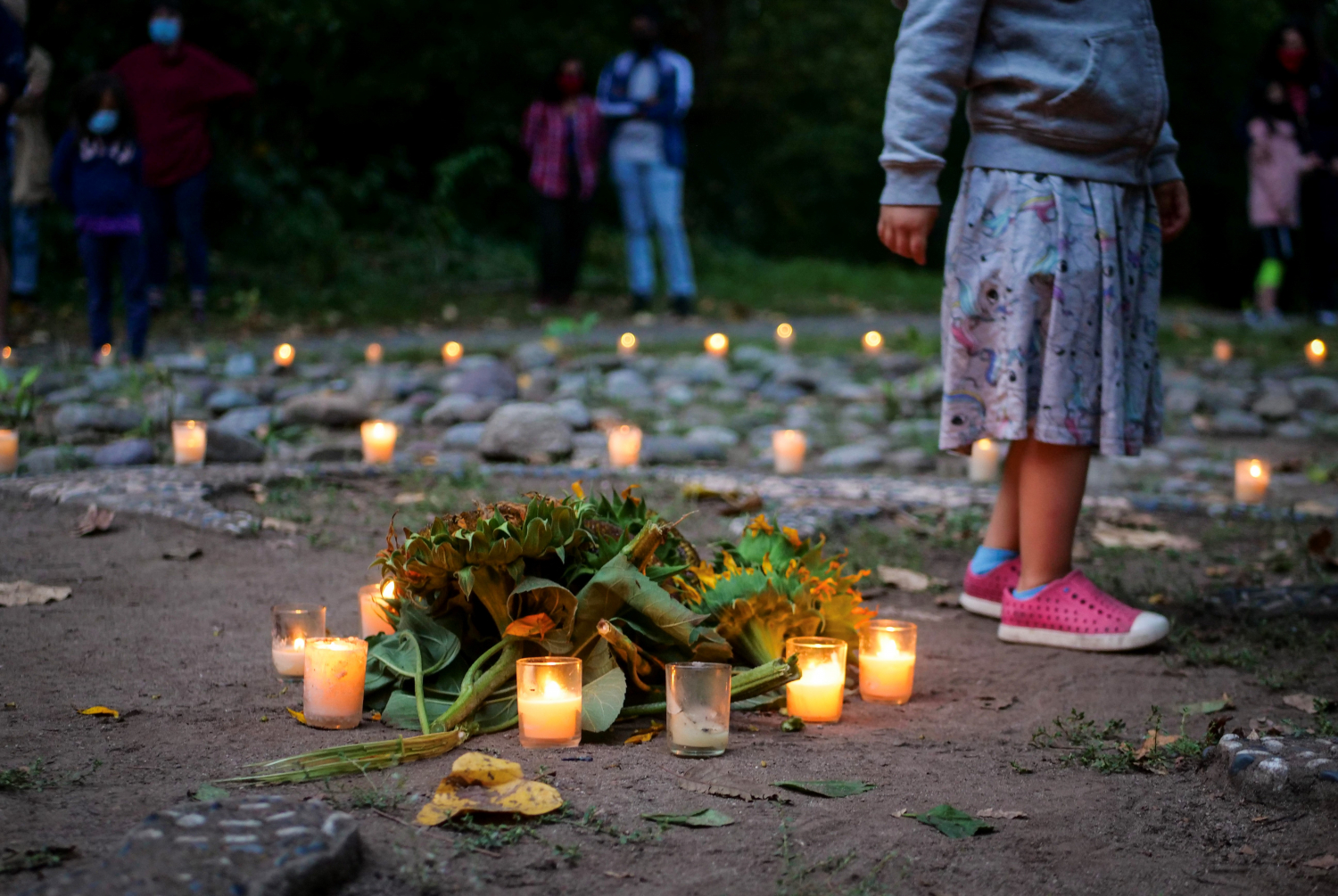 Still Moon_0 A pile of sunflower heads on the ground, surrounded by lit tealights, with more lit tealights and people in the background
